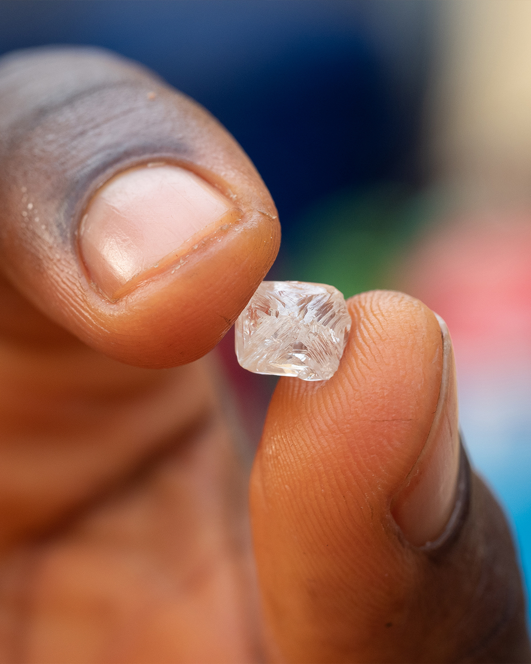 A close-up of a hand holding a raw, uncut diamond from artisanal mining in Sierra Leone